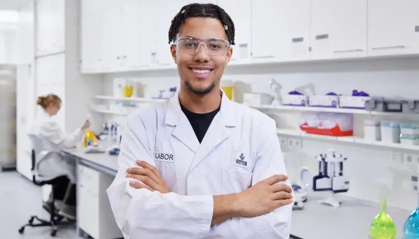 Junger Mann im Chemielabor, bereit für neue chemielaborant stellenangebote. Im Hintergrund eine Kollegin bei der Arbeit.