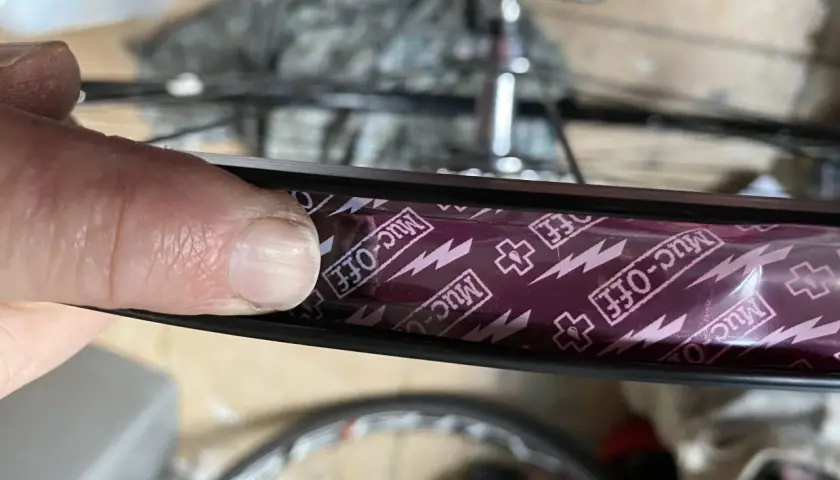 Close-up of a finger pressing down on Muc-Off tubeless rim tape, showing the process of how to tape tubeless rims for a secure seal.