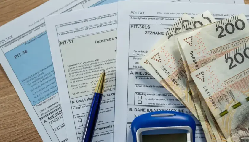 Formularze podatkowe PIT, długopis, kalkulator i banknoty 200 zł. Czas na rozliczenie podatku, zbliża się ikze limit 2026.