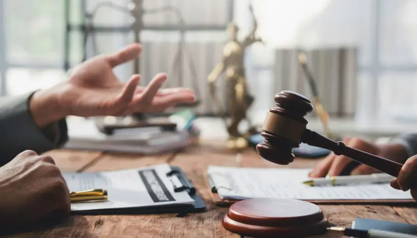 Dwie osoby przy drewnianym stole, jedna gestykuluje, druga trzyma młotek sędziowski. W tle waga sprawiedliwości i Statua Temidy. Pytanie: ile czasu ma sąd na wysłanie uzasadnienia wyroku?