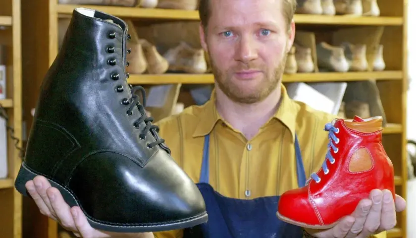 Schuhmacher hält einen schwarzen und einen roten Schuh, die für Klumpfuß-Kinder gefertigt wurden.