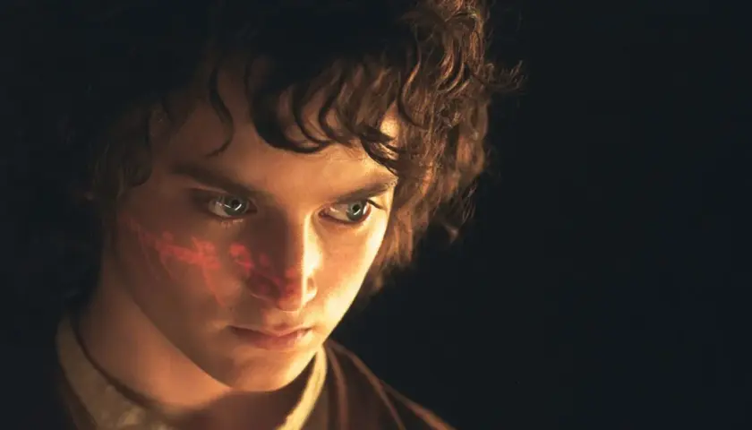 Elijah Wood, kto gra Frodo Bagginsa, z czerwonym znakiem na policzku, w ciemności.
