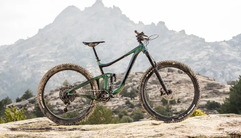 A 2020 Giant Reign mountain bike rests on a rocky outcrop, ready to conquer the rugged, misty mountains in the background.