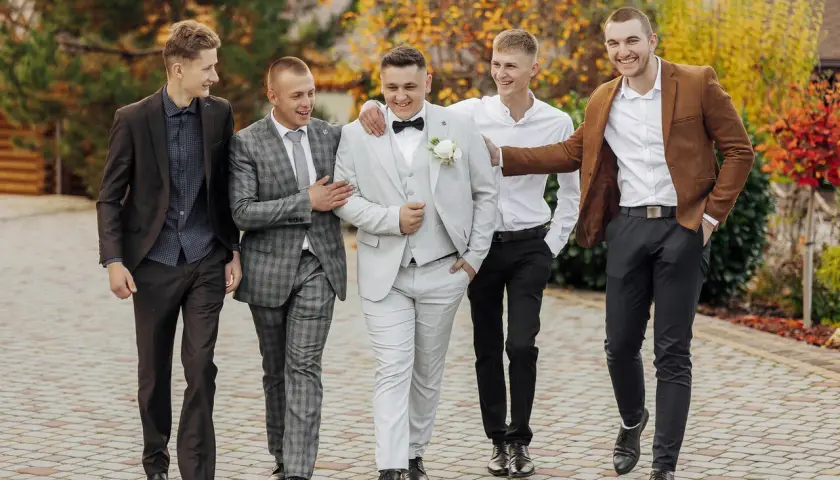 Pięciu mężczyzn w eleganckich garniturach idzie razem. Inspiracja, jak ubrać się na wesele mężczyzna.