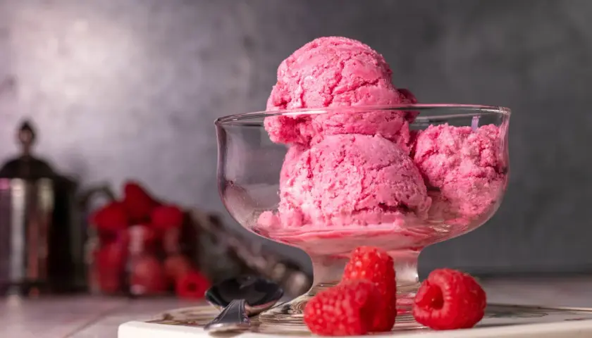 Ein Glas mit cremigem, veganem Himbeereis, garniert mit frischen Himbeeren. Perfekt für einen heißen Sommertag.