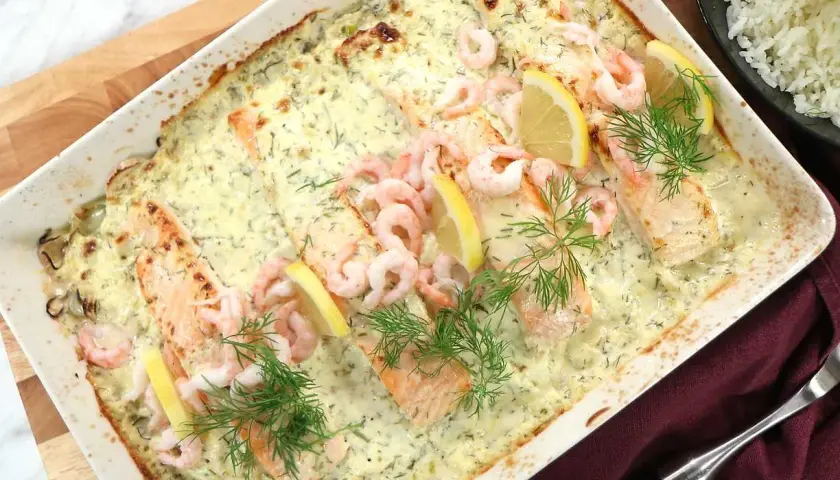 Lax med apelsinsås, toppad med räkor och citronklyftor, serveras i en ugnsform. Dillkvistar ger en fräsch touch.