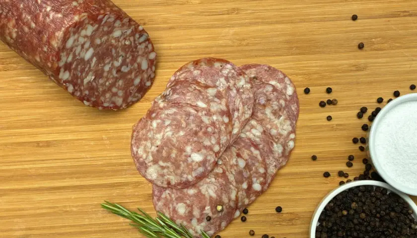 Kawałek salami napoli i kilka plastrów na desce z rozmarynem, pieprzem i solą.