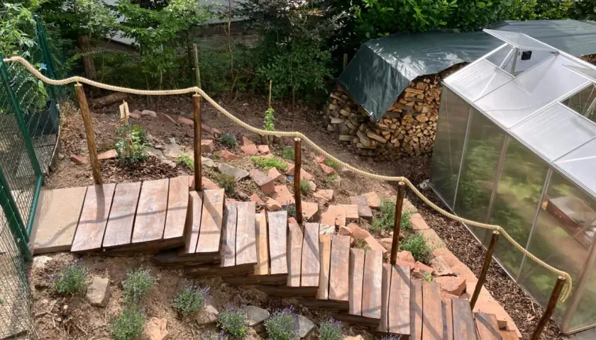 Eine **einfache Gartentreppe selber bauen** ist hier gelungen. Holzstufen führen durch Lavendel und Steine, ein Seilgeländer sorgt für Halt.