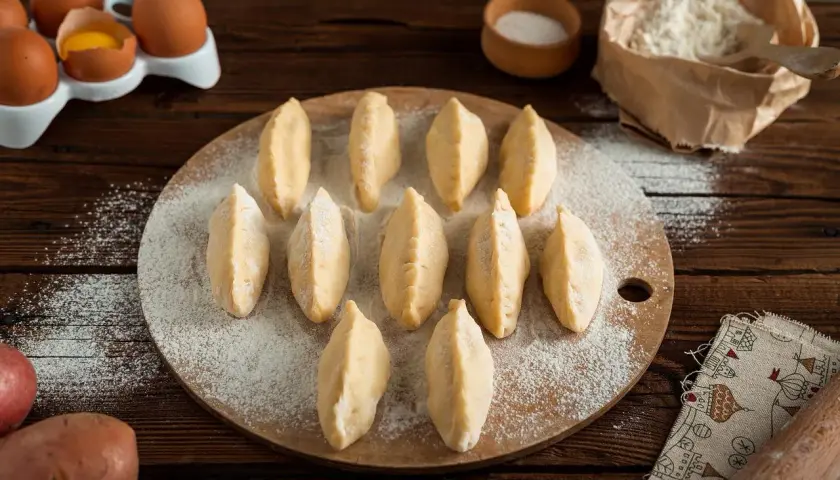 Gotowe do lepienia pierogi na desce, obok jajka i mąka. Czy ciasto na pierogi można zamrozić? Tak, to świetny sposób na zapas!