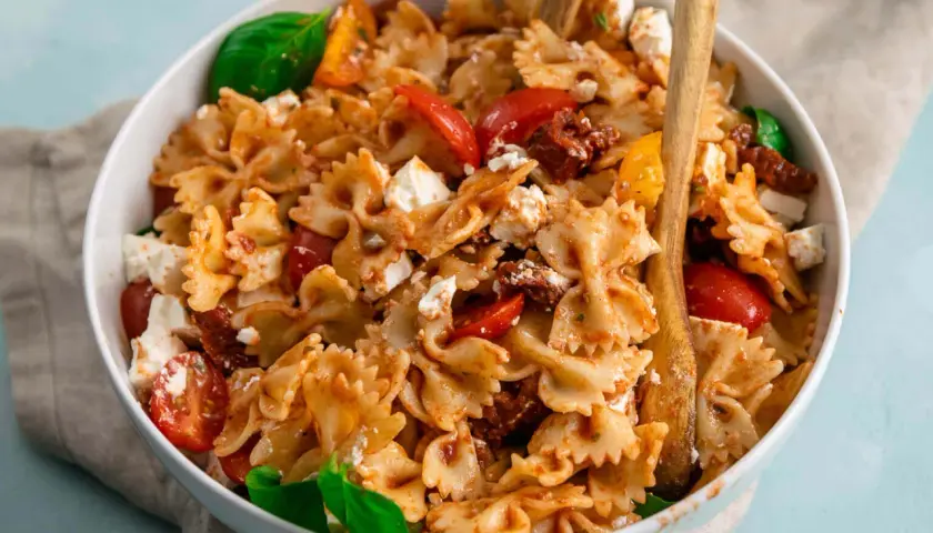 Farfalle-Nudelsalat mit frischen Tomaten, Mozzarella und sonnengetrockneten Tomaten, garniert mit Basilikum.