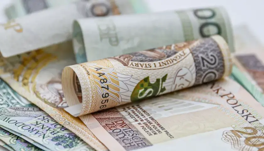 Zwijane polskie banknoty, w tym 20 złotych, symbolizują oszczędności na dodatkowy urlop.
