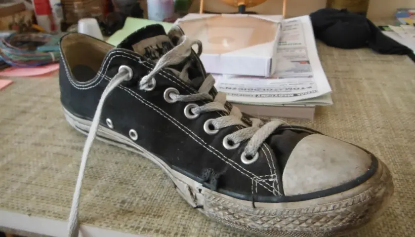 Une chaussure Converse noire usée, avec la semelle qui se décolle, témoigne de nombreuses aventures.