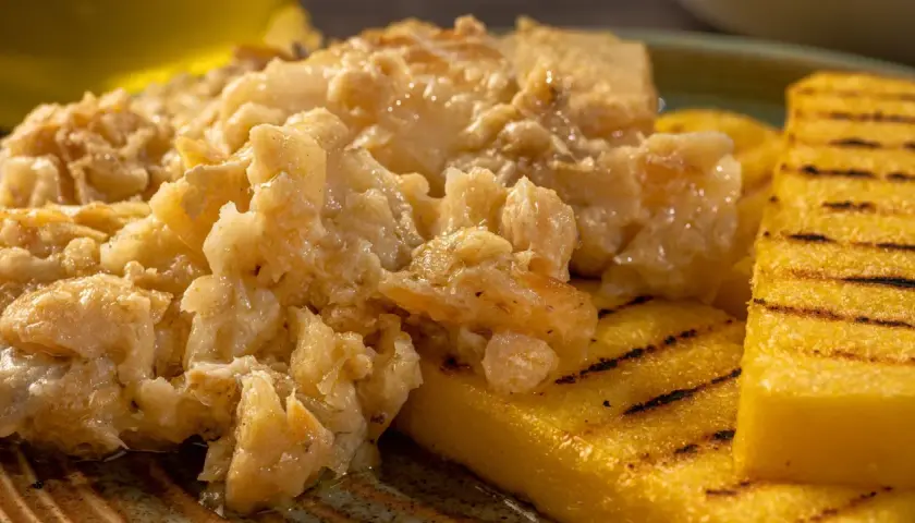 Un saporito baccalà alla vicentina, cremoso e profumato, servito su fette di polenta grigliata.