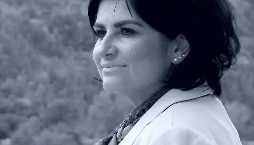 Portret Agnieszki Kołacz Leszczyńskiej w białej marynarce, z delikatnym uśmiechem i ozdobnymi kolczykami.