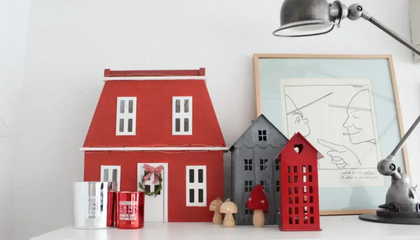 Un pueblo de casitas de navidad de madera, con una casa roja grande y otras más pequeñas, adornos y velas.