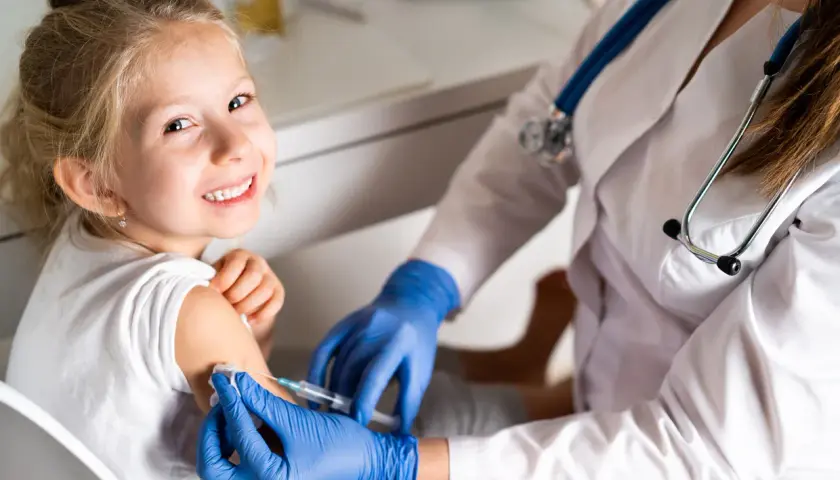 Niña sonriente recibe vacuna contra la gripe. Es recomendable vacunar a los niños de la gripe para proteger su salud.