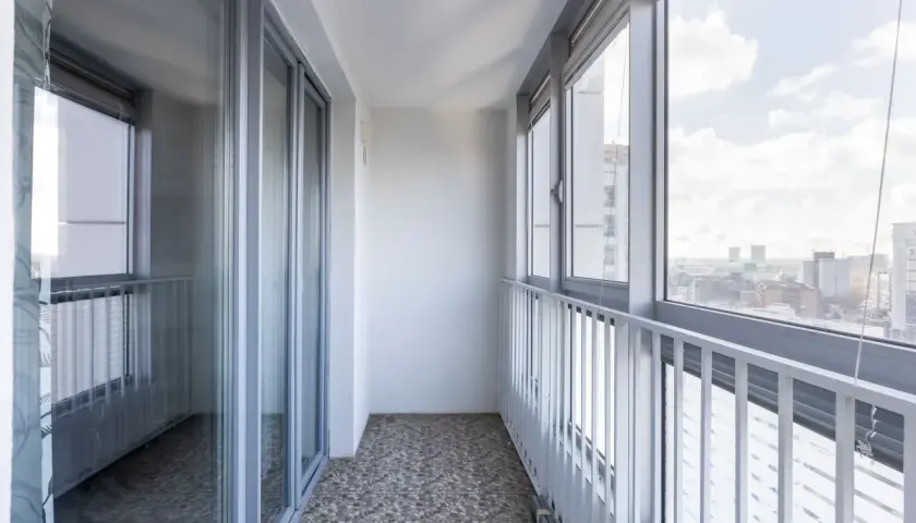 Szare okna i drzwi balkonowe, biała balustrada i widok na miasto. Idealne miejsce, by zastanowić się, czym osłonić balkon.