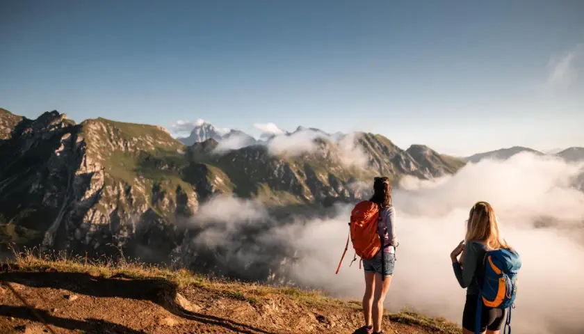 Zwei Frauen mit Rucksäcken genießen den Ausblick nach einem erfolgreichen Rosskopf Wandern. Wolken ziehen durch die Berge.