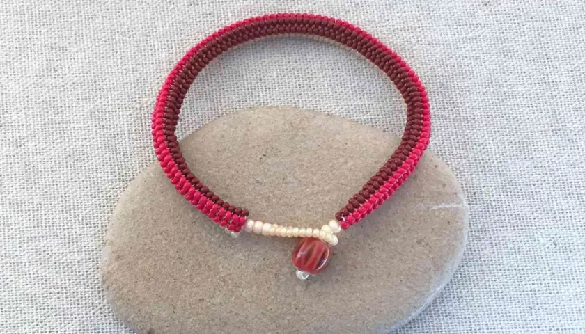 Braccialetto fatto a mano con nodi per braccialetti elastici, perline rosse e marroni, e una perlina centrale striata.