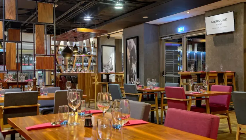 Elegancka restauracja w hotelu Mercure Wrocław Centrum. Drewniane stoły, czerwone i szare krzesła, półki z winami.