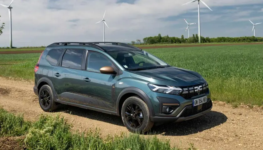 Dacia Jogger verde su sterrato, con pale eoliche sullo sfondo. Un'auto perfetta per un viaggio in autostrada con **GPL**.