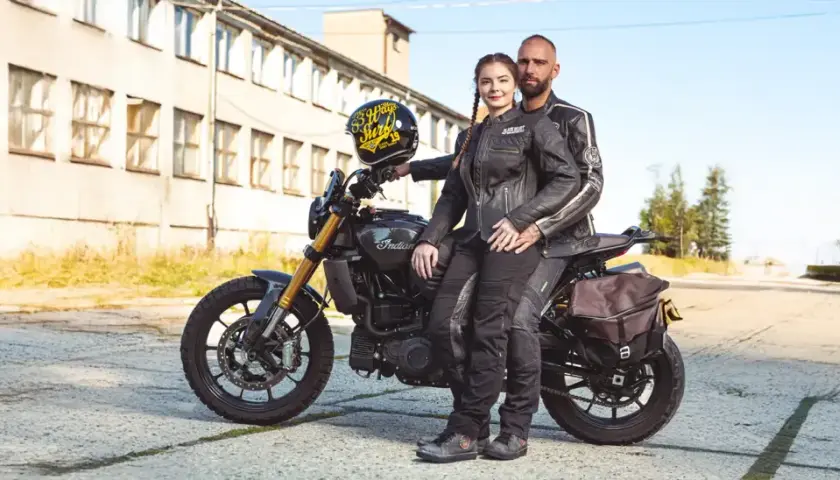 Para motocyklistów w skórzanych ubraniach siedzi na motocyklu Indian, obok stoi kask.