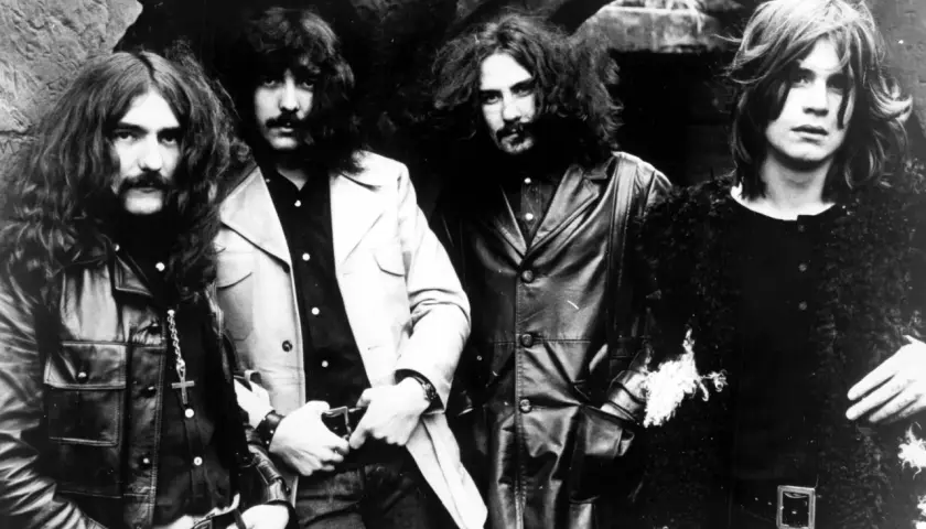 Czterech muzyków Black Sabbath, w tym wokalista, pozuje do zdjęcia w rockowych strojach.