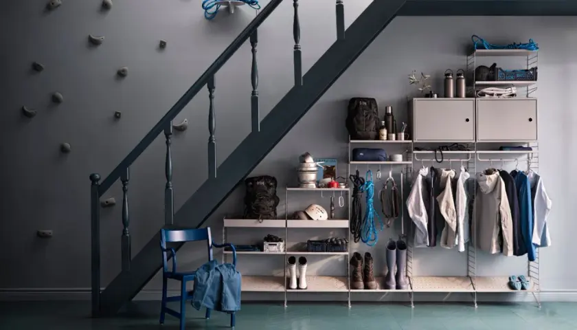 Praktische Garderobe unter der Treppe mit Klettergriffen an der Wand, Jacken, Rucksäcken und Stiefeln.