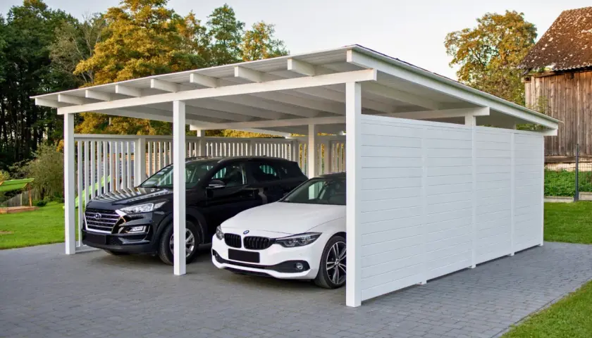 Nowoczesna budowa wiaty chroni dwa samochody: czarnego SUV-a i białe BMW. Elegancka konstrukcja z białymi panelami i dachem.