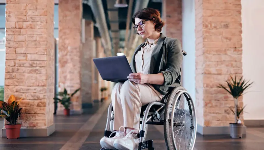 Kobieta na wózku inwalidzkim pracuje na laptopie w nowoczesnym biurze. Zlecenie na wózek inwalidzki zostało zrealizowane.