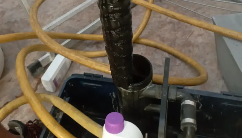 Czarna, brudna rura i żółty wąż wskazują na płukanie instalacji grzewczej. Widać też butelkę z preparatem.