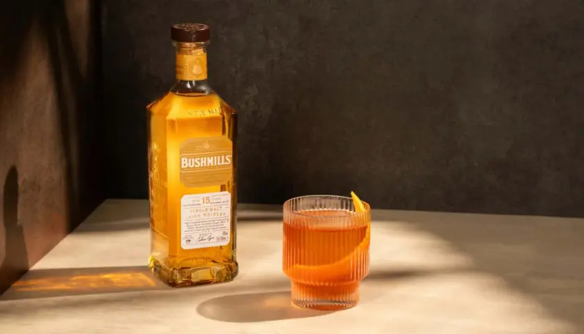 Butelka Bushmills 15 Year Old Single Malt Irish Whiskey obok szklanki z drinkiem. Wiele pozytywnych bushmills whisky opinie potwierdza jego wyjątkowy smak.