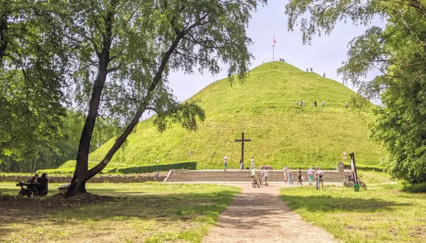 Zielony Kopiec Piłsudskiego z krzyżem i ludźmi spacerującymi po zboczu.