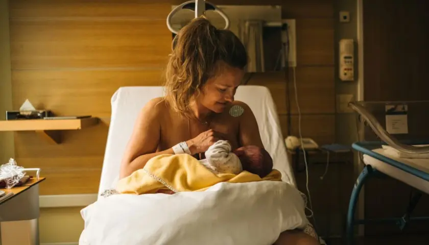 En mamma ammar sitt nyfödda barn på en sjukhussäng. En lugn stund efter förlossningen, kanske inför en efterkontroll på MVC.