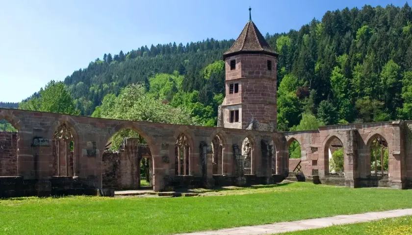 Ruinen eines evangelischen Klosters mit einem Turm im Hintergrund, umgeben von grünen Hügeln und Bäumen.