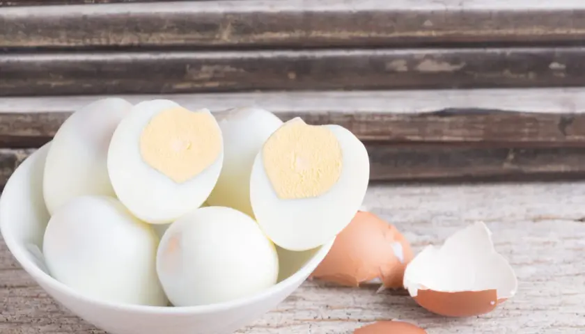 Un bol de blancs d'œufs durs, certains coupés en deux, prêts pour la conservation. Des coquilles d'œufs brisées à côté.