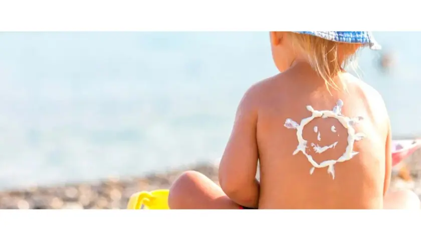Bambino con crema solare a forma di sole sulla schiena, al mare. Protezione per la dermatite atopica e il sole.