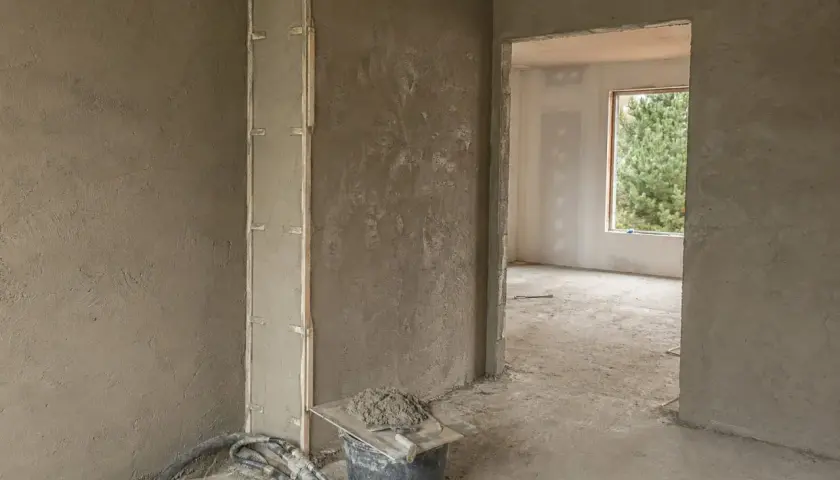 Ściany pokryte tynkami gipsowymi, widoczny fragment pionowej konstrukcji z listwami. W wiadrze zaprawa i kielnia.