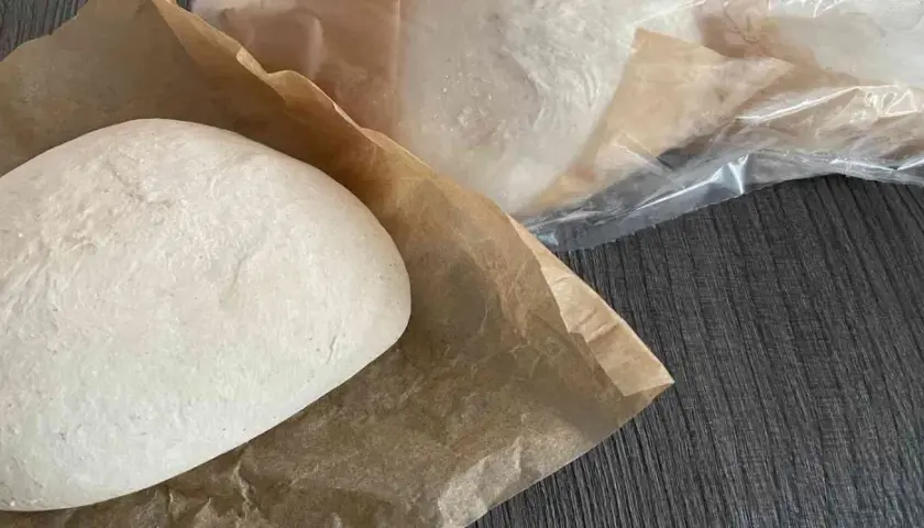 Frische Pizzaböden, bereit für das Pizzateig einfrieren. Einer liegt auf Backpapier, weitere sind in Folie verpackt.