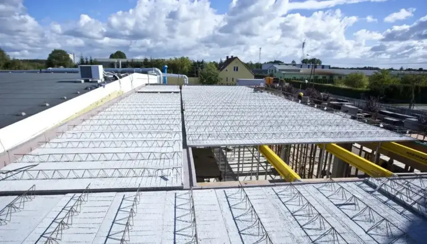 Budowa nowego stropu nad halą przemysłową. Metalowe kratownice i zbrojenie czekają na beton.