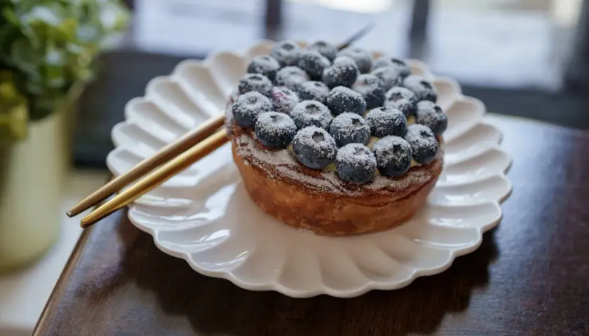 Tarte myrtille Savoie, une gourmandise aux myrtilles fraîches saupoudrée de sucre glace, servie sur une assiette blanche.