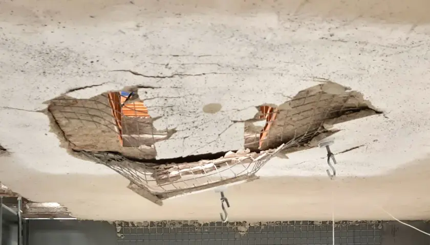 Soffitto sfondato che rivela la struttura del solaio sottostante, con mattoni e armatura a vista.