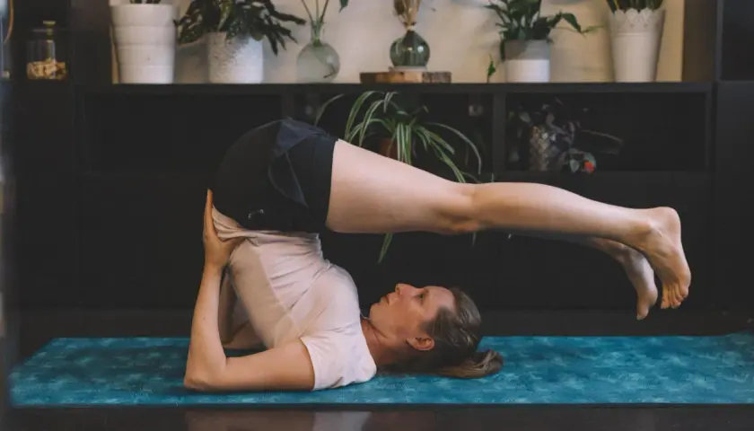 Femme effectuant des étirements du dos sur un tapis de yoga bleu. Ses jambes sont levées et tendues au-dessus de sa tête.