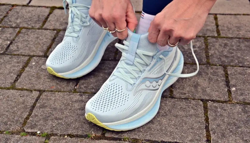 Dłonie zawiązują sznurówki jasnoniebieskich butów do biegania Saucony Ride 18 na chodniku z kostki brukowej.