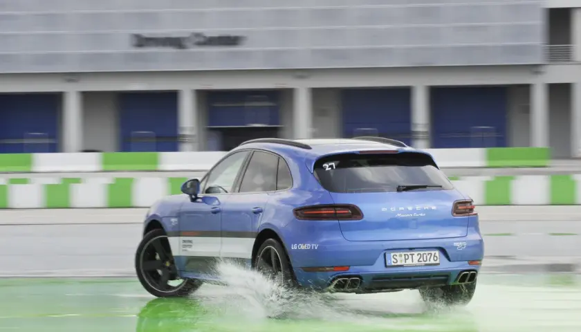 Niebieski Porsche Macan Turbo na mokrym torze Driving Center, rozpryskuje wodę. DSC co to? System stabilizacji toru jazdy.