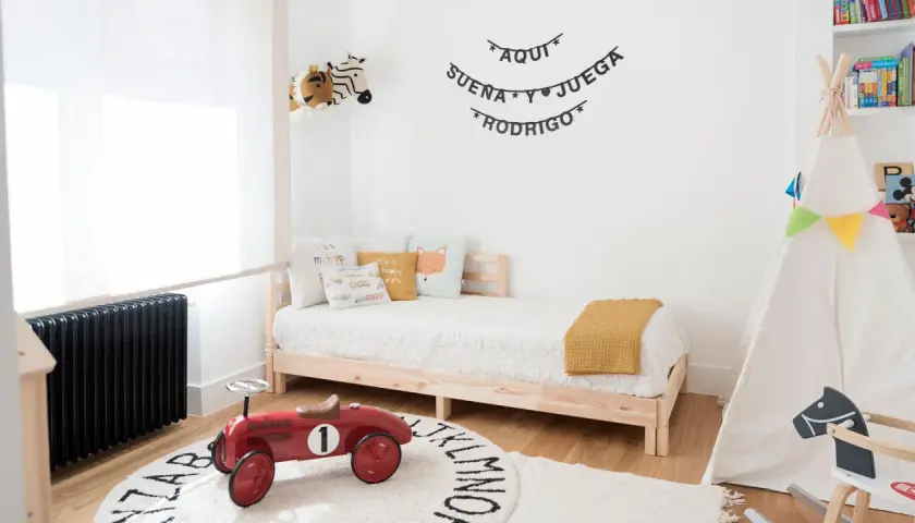 Un cuadro juego de niños con un tipi, cama, peluches y un coche de juguete rojo. "Aquí sueña y juega Rodrigo" decora la pared.