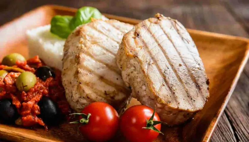 Delizioso tonno alla piastra con contorno di riso, pomodorini, olive e basilico su un piatto di legno.