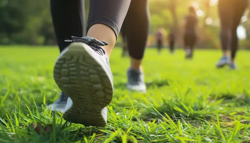 Grupa osób uprawia power walking po zielonej trawie w parku, w promieniach zachodzącego słońca.
