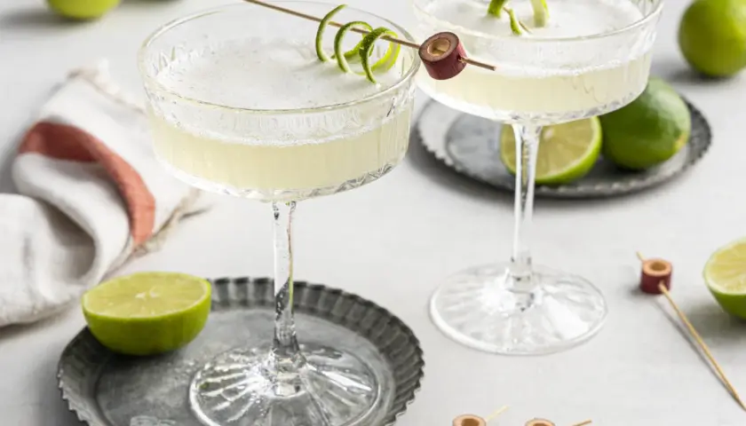 Zwei erfrischende Daiquiri Cocktails mit Limettenschale garniert, umgeben von frischen Limetten.