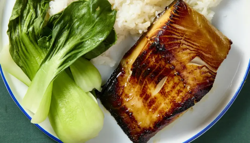 A glistening piece of black cod, marinated and seared to perfection, sits beside fluffy white rice and vibrant green bok choy.